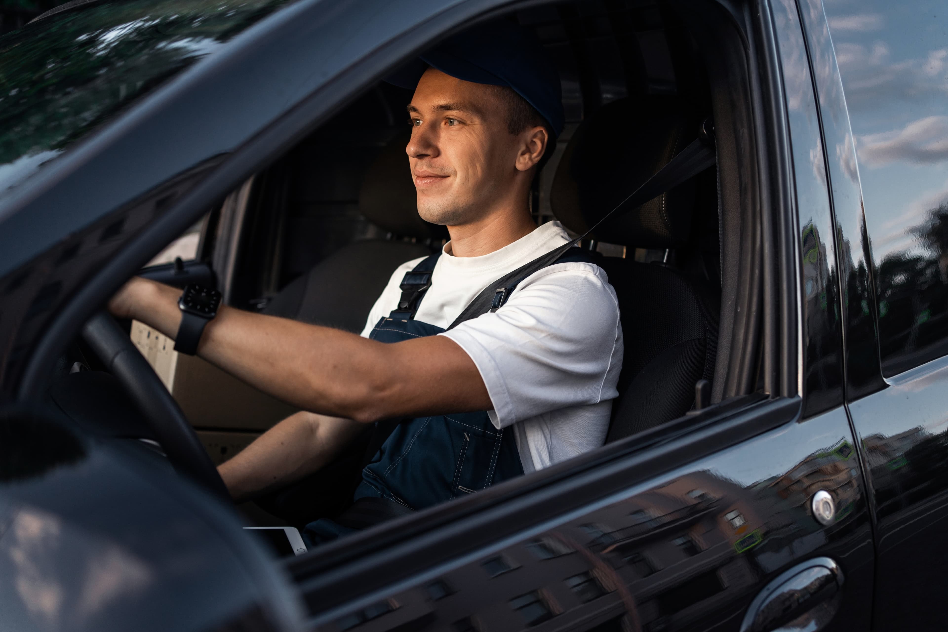 Mann in Latzhose in Auto am Lenkrad.
