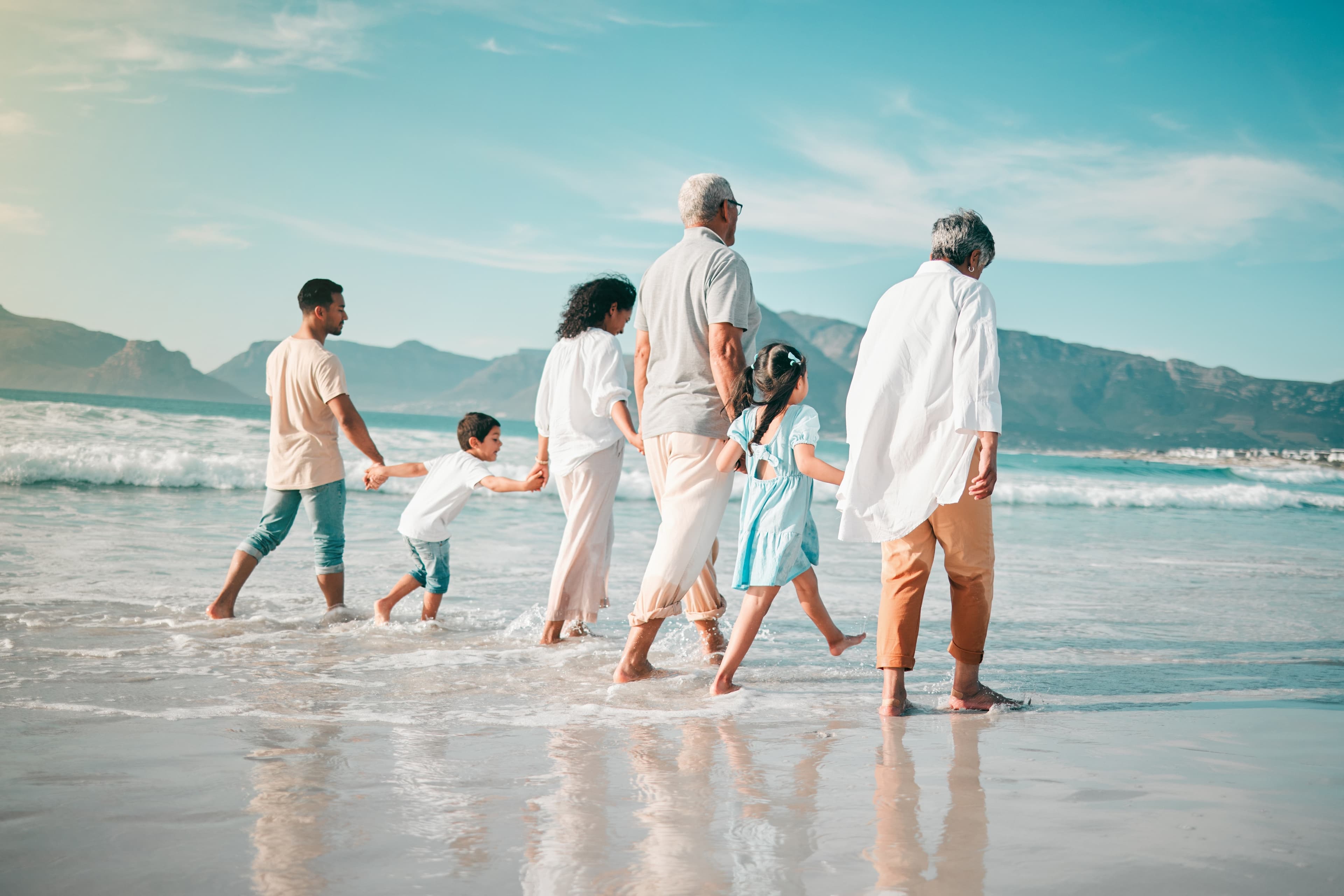 Familie mit 6 Personen geht Hand in Hand am Meer spazieren.