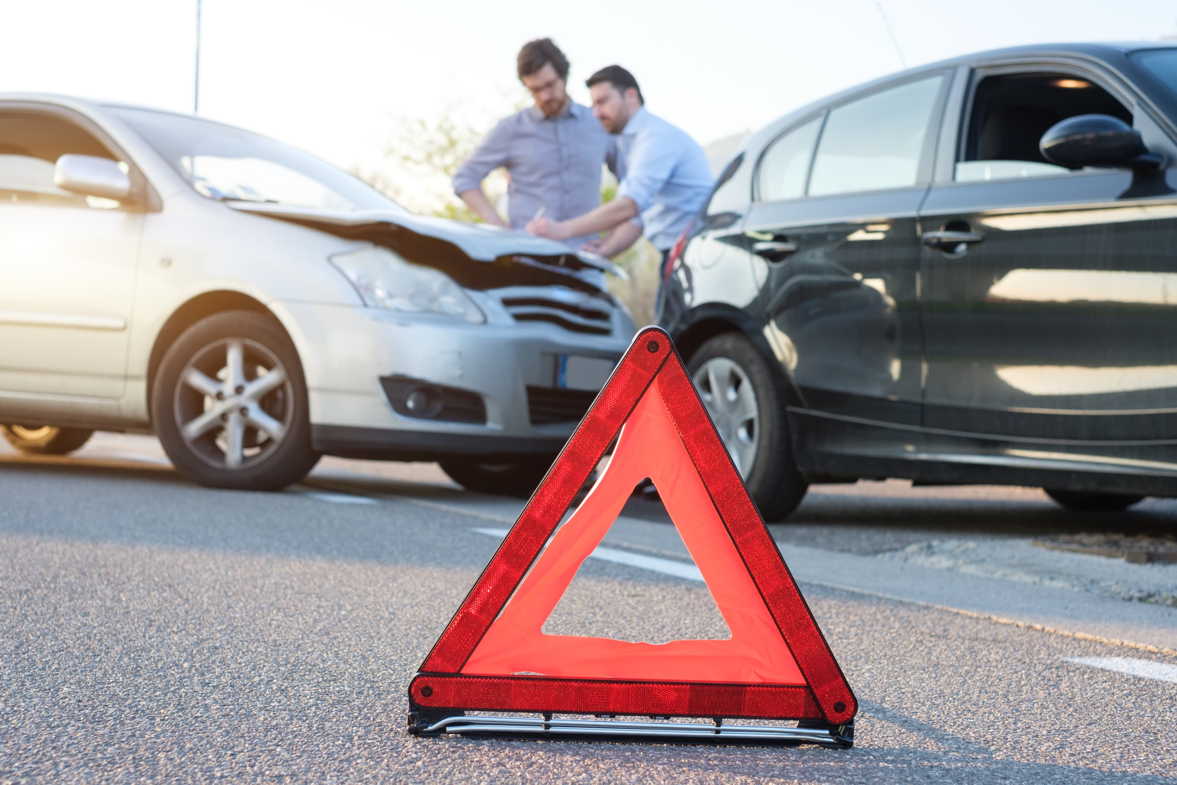 Warndreieck im Vordergrund auf Straße. Im Hintergrund zwei Autos mit Schaden.