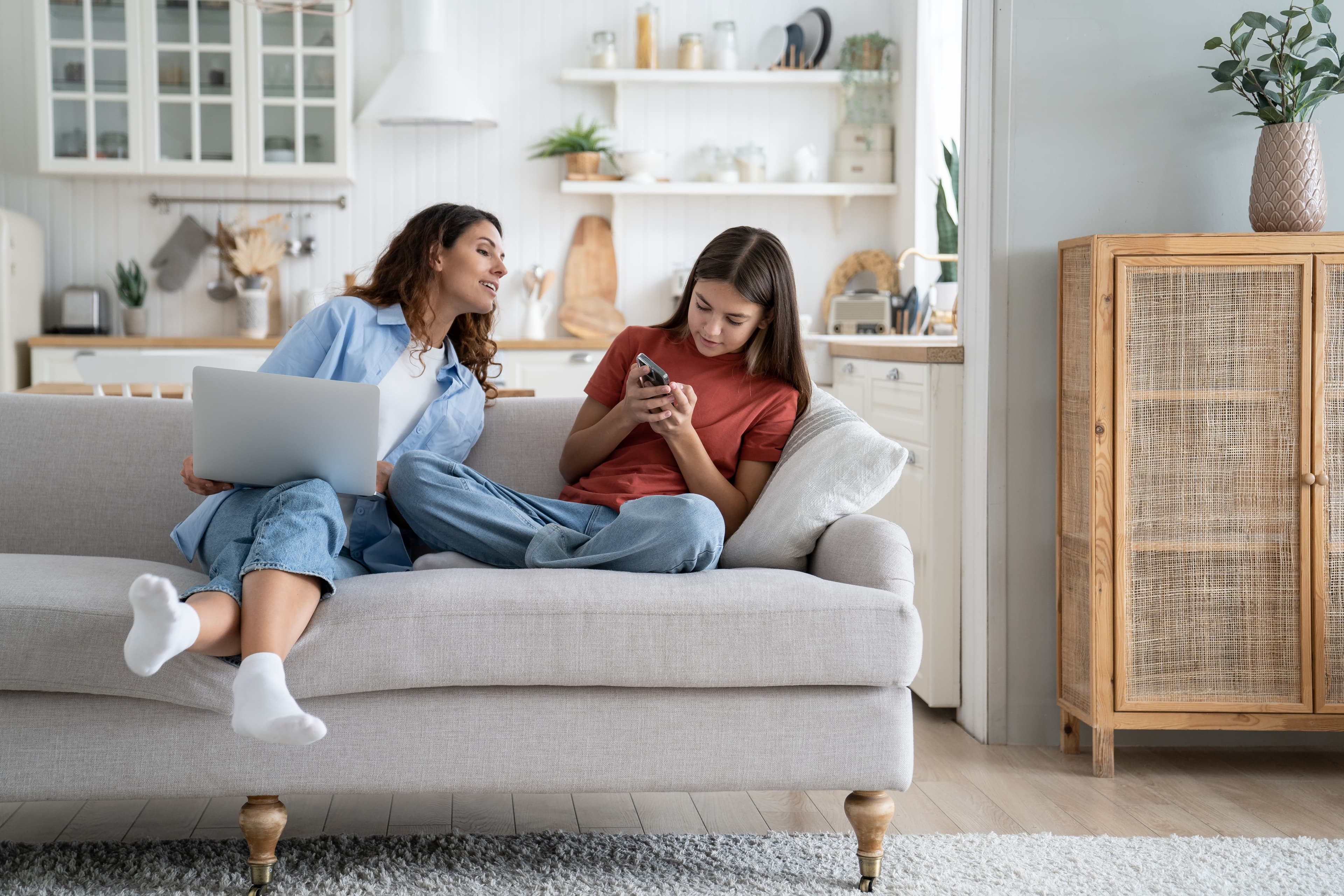 Zwei Frauen sitzen auf Sofa mit Laptop und Handy.