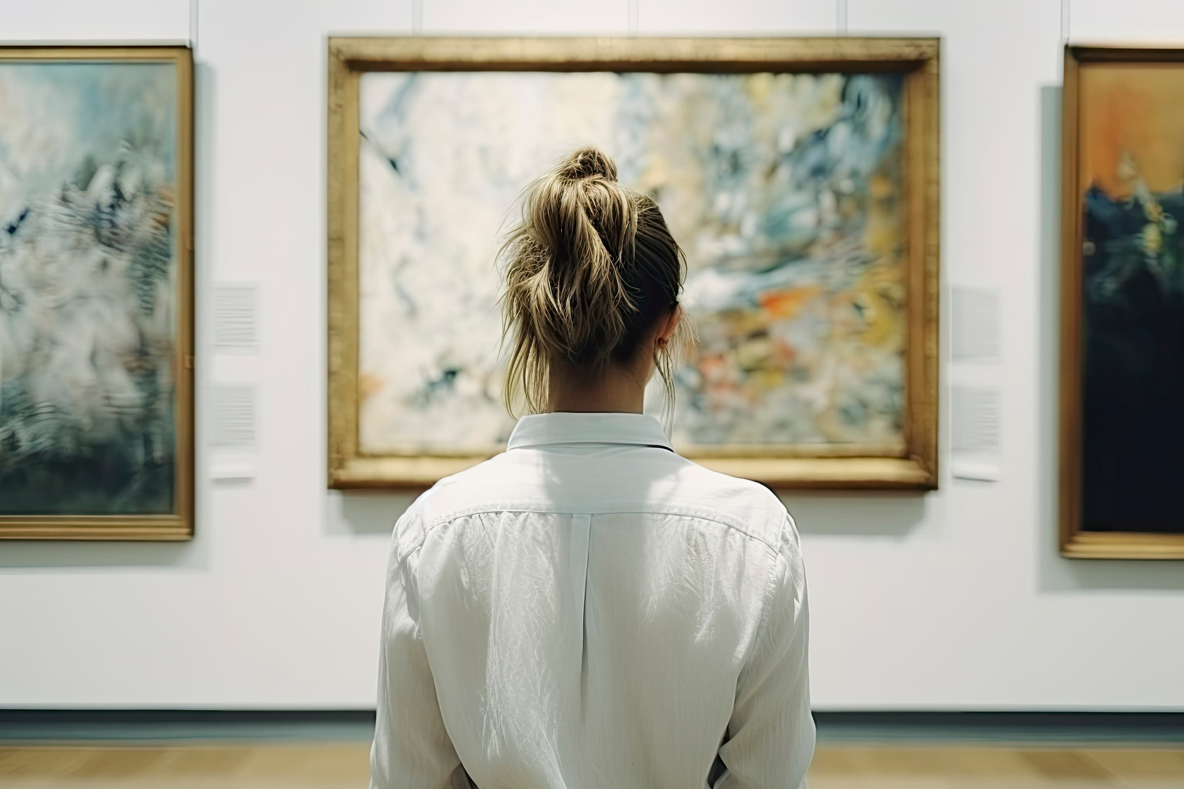 Frau mit Rücken zur Kamera steht vor Gemälden in einer Ausstellung.