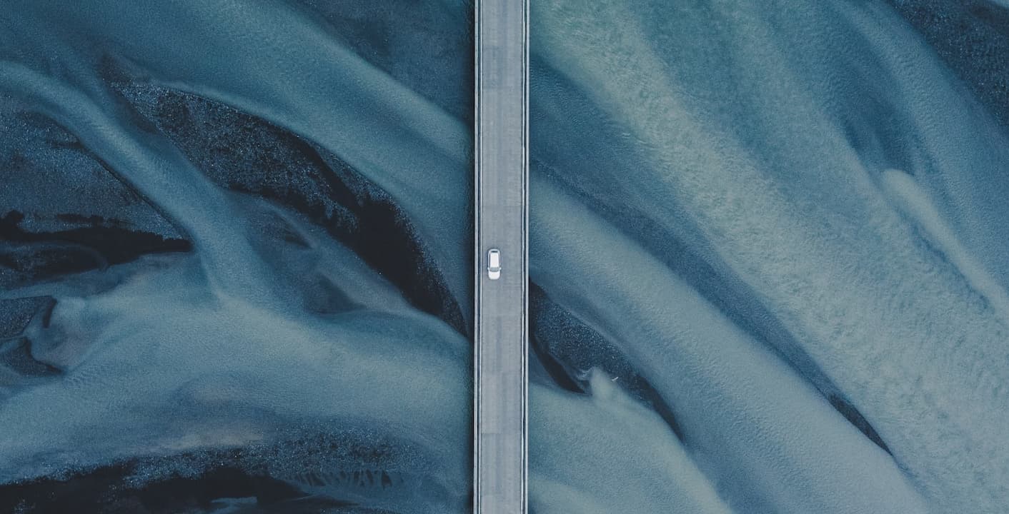 Straße verläuft senkrecht durch das Bild mit einem Auto. Hintergrund blaue Natur.