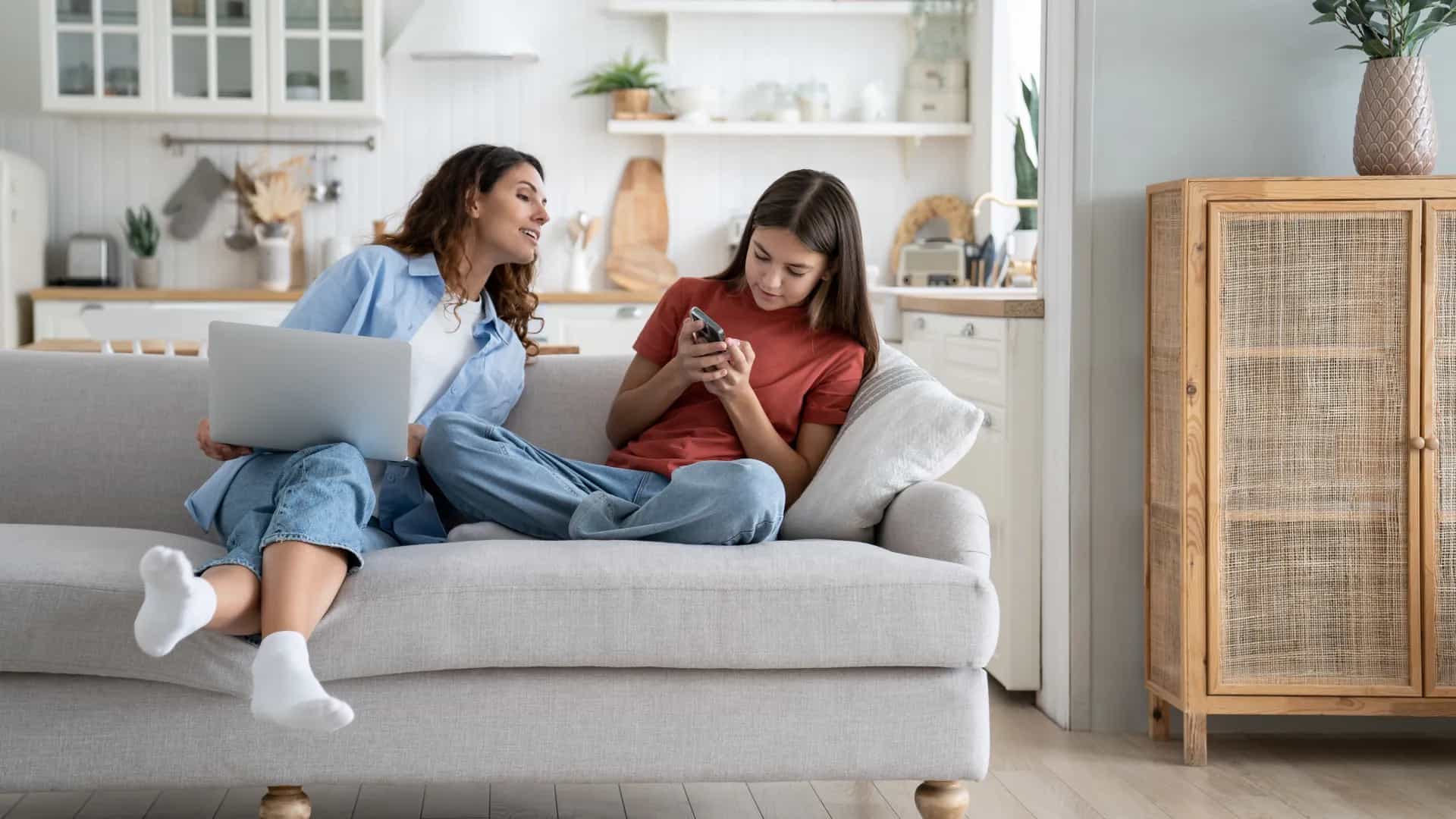 Zwei Frauen sitzen auf Sofa mit Laptop und Handy.